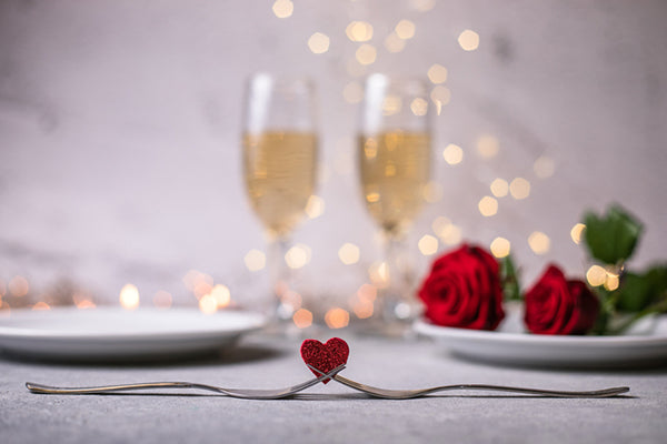 Forks and a heart on a dinner table with a plate of roses and drinks blurred in the background